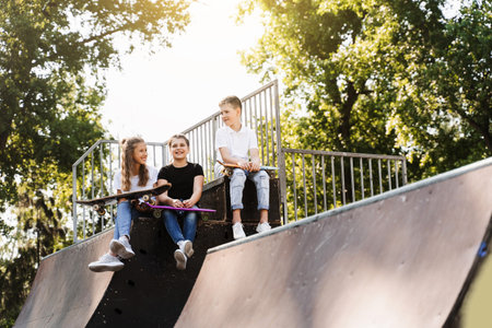 Phone addicted sports kids with skateboard and penny boards are sitting and looking at smartphones...