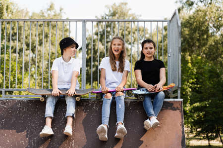 Phone addicted sports kids with skateboard and penny boards are sitting and looking at smartphones on sports ramp on playground. Children addiction of phones.の写真素材