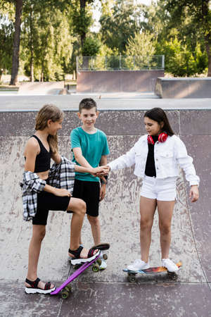 Phone addicted sports kids with skateboard and penny boards are sitting and looking at smartphones on sports ramp on playground. Children addiction of phones.の写真素材