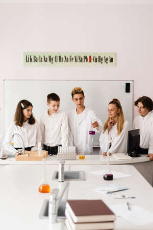 School chemistry teacher shows children flasks with liquids for experiments in the laboratory. Education concept. Group lesson of classmates at chemistry lessonの写真素材