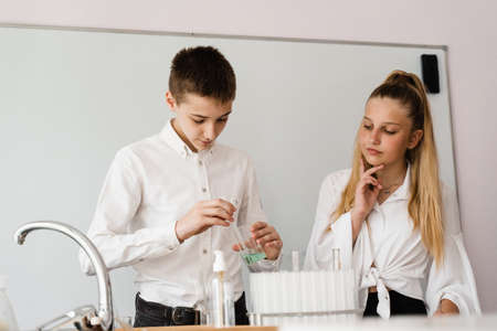 Pupil holding flask with liquid for experiments in laboratory. Education concept. Group of pupils studying chemistry lesson in schoolの写真素材