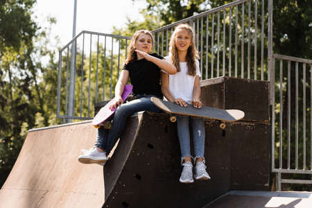 Kids girls smile and laugh and have fun together. Children with skateboard and penny boards communicate and discuss on the sports playground. Girls friendship conceptの写真素材
