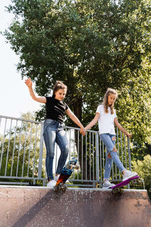 Children girls skating together. Friendship. Friends ready for ride on penny board on skateboard park playground. Sports equipment for kids. Extreme lifestyleの写真素材