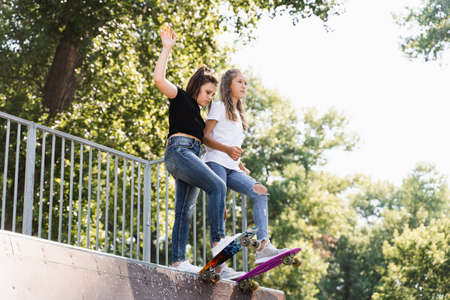 Skater children girls reade to ride on penny board on skate sport ramp at sunset together. Sports...