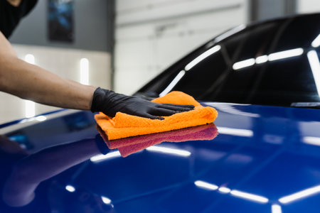 Hand car drying with microfiber in detailing auto service. Cleaner worker dry body car after washing...