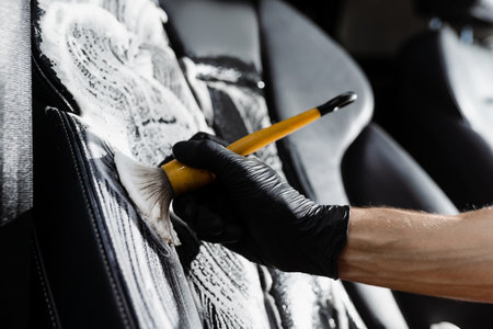 Foam cleaning black leather seat using brush. Worker in auto cleaning service clean car inside. Car interior detailingの写真素材