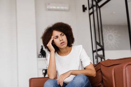 Depressed girl with migraine headache. Sad african american woman touches temples because of stress and despair in her life. Problems in lifeの写真素材