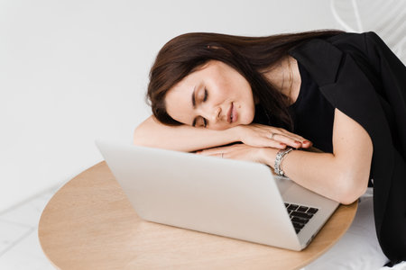 Sleeping girl with laptop on the table on white background. Tired young woman have a break at work and sleeping and relaxing at laptop on workplace due to overtime workの写真素材