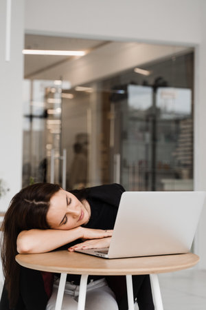 Girl with closed eyes have a break at work and sleeping and relaxing at laptop on workplace due to overtime workの写真素材
