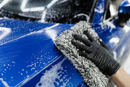Hand washing with microfiber glove with foam car body in garage. Car washer doing manual foam...