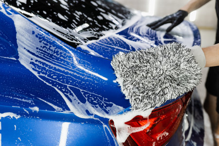Car washer doing manual foam washing in auto detailing service. Hand washing with microfiber glove...