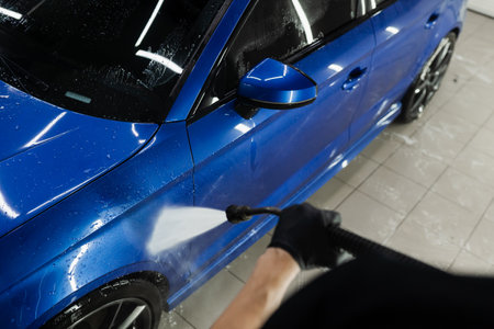 Car washer pouring water for full body car wash. Spraying water on car to wash off foam in the garage. Process of detailing washing in car serviceの写真素材