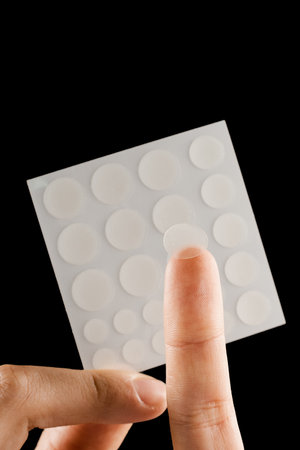 Close-up round acne patch on finger and set of patches in hands on black background. Acne patches for treatment of pimple and rosacea close-up. Facial rejuvenation cleansing cosmetologyの写真素材