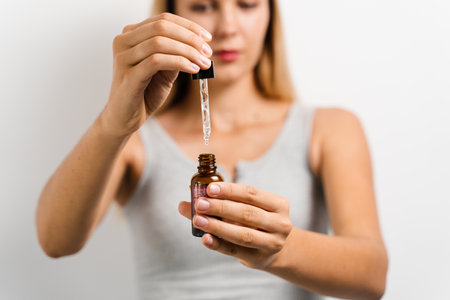 Girl holding pipette with oil facial serum in hands for acne treatment and wrinkle smoothing. Girl with face serum making beauty procedure on white backgroundの写真素材