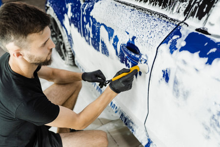 Hand brush washing of car body with foam in car detailing service. Car wash worker washes a car bodyの写真素材