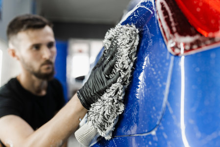 Car washer doing manual foam washing in auto detailing service. Hand washing with microfiber glove with foam car body in garageの写真素材