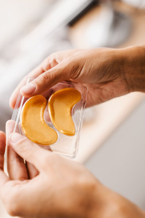 Golden hydrogel eye patches with peptides and hyaluronic acid in hands. Close-up set of gold pathes for smooth out fine wrinkles, remove swelling or bags under the eyesの写真素材