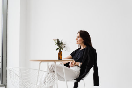 Happy confident woman is sitting at table on white background indoor in cafe. Smiling young woman dressed casual business style enjoy her lifestyleの写真素材