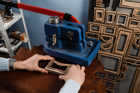 Process of creating genuine leather products in factory. Craftsman is using leather punching press for creating forms from genuine leatherの写真素材