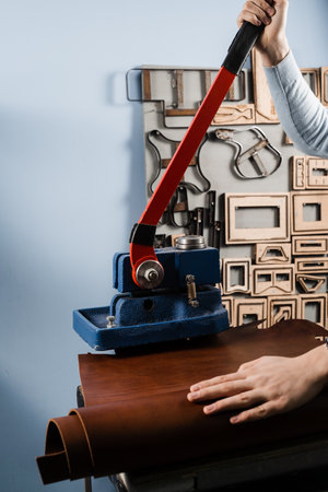 Craftsman is using leather punching press for creating forms from genuine leather. Process of...