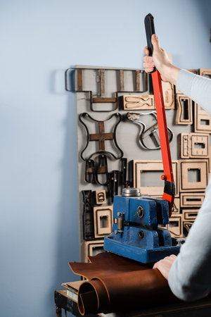 Craftsman is using leather punching press for creating forms from genuine leather. Process of creating genuine leather products in factoryの写真素材