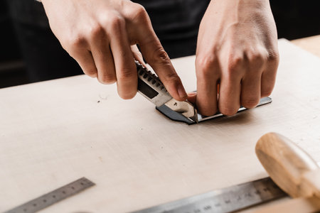 Process of cutting genuine leather. Craftsman is cutting genuine leather using cutter knife for creation natural leather products. Equipment for genuine leather production in workshopの写真素材