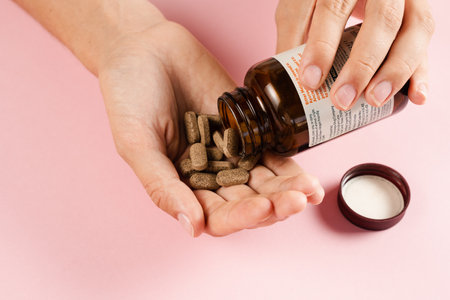 Tablets of dietary supplements in hand for daily pills intake on pink background. Set of zinc pills, antioxidants from aging, lecithin and adaptogenの写真素材