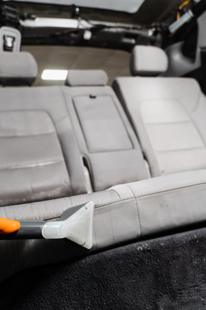 Car cleaner is extracting dirt from car seat using dry cleaning extractor machine. Cleaning textile seats in car interior using extractor machine for dry cleanの写真素材