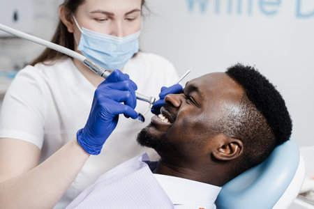 Dentist with dental drill treats african man in dentistry clinic. Dental filling for african american man patientの写真素材