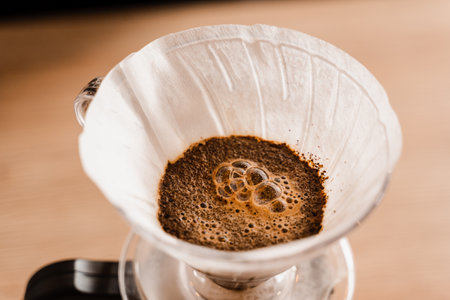 Pour over filter with ground coffee in the funnel in focus. Drip filter coffee brewing. Pour over alternative method of pouring water over roasted and ground coffee beans contained in filterの写真素材