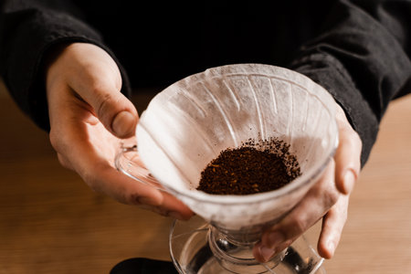 Barista holding pour over device with ground coffee on paper filter before pouring water from drip...