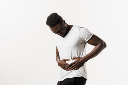 Sick african american man is holding his stomach because it hurts. Pancreatitis disease of pancreas becomes inflamed. Cancer of stomach and esophagus of African manの写真素材