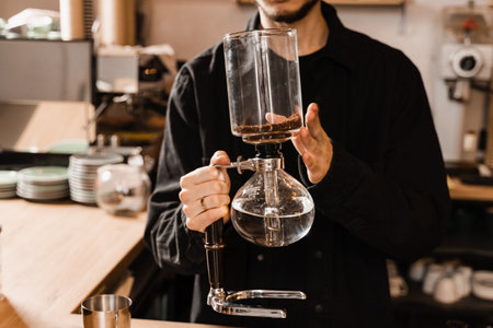 Barista is holding siphon before starting boiling water inside syphon. Process of brewing siphon coffee in cafeの写真素材