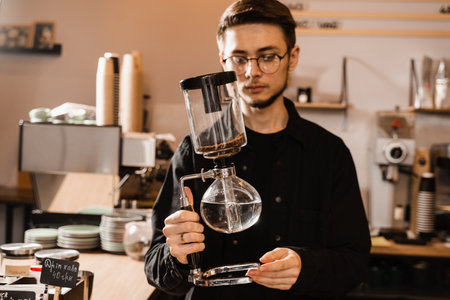 Barista is holding siphon before starting boiling water inside syphon. Process of brewing siphon coffee in cafeの写真素材