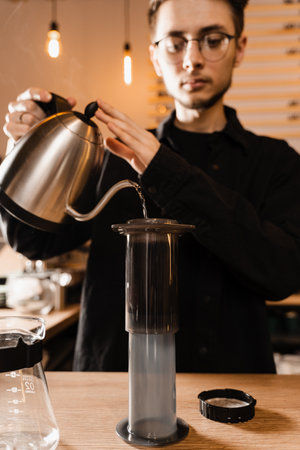 Barista is pouring hot water from drip kettle to aeropress. Process of brewing aeropress. Pouring hot water over roasted and ground coffee beans in aeropressの写真素材