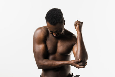Sport traumatology. Elbow injury of muscular african american man on white background. African american man with pain and bruise in his arm due to an accidentの写真素材