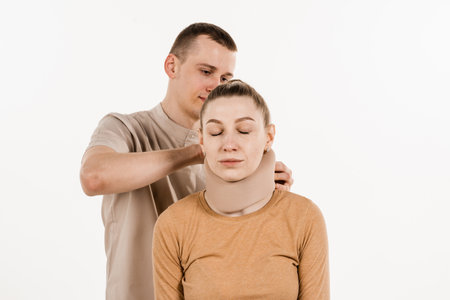 Neurosurgeon puts neck bandage on girl to stabilize the cervical region in case of neck pain, injuries and sprains on white backgroundの写真素材