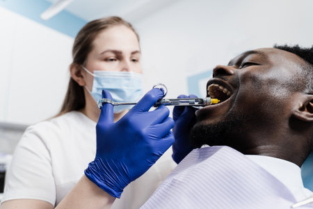 Dentist injects anesthesia syringe of the diseased teeth for the african man patient. Caries treatmentの写真素材