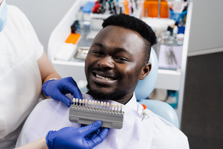 Teeth whitening of african man. Dentist working with teeth color shades guide. Dentistry. Doctor checking teeth color matching samples in dental clinicの写真素材