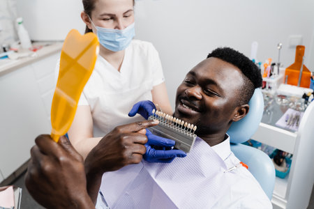 Dentistry. Doctor checking teeth color matching samples in dental clinic. Teeth whitening of african man. Dentist working with teeth color shades guideの写真素材