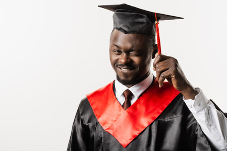 Portrait of graduate african man graduated from university and got master degree. Graduation. Happy african man in black graduation robe is smiling on white backgroundの写真素材
