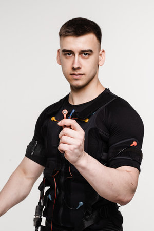 Muscular male athlete in EMS suit with contactor in hand that uses electrical impulses to stimulate muscles on white background. Sport training in electrical muscle stimulation suitの写真素材