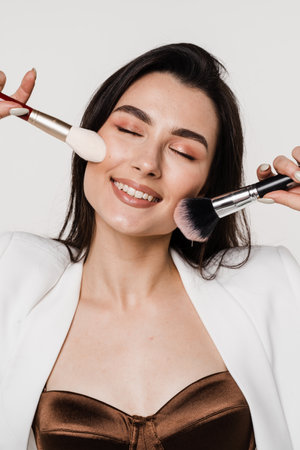 Professional make-up artist with makeup brushes on white background. Attractive girl is holding eye shadow brushes and smilingの写真素材