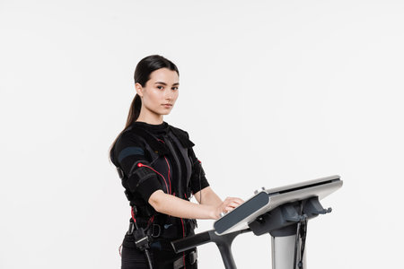 Fit girl in EMS suit on white background. Sport training in electrical muscle stimulation suit