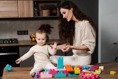 Child daughter is playing in bricks constructor with mom together. Mother and her kid spend time at home togetherの写真素材
