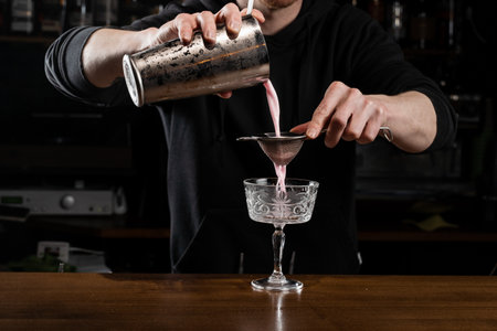 Bartender is pouring pink Clover club alcoholic cocktail in the glass. Bartender mixes egg white,...