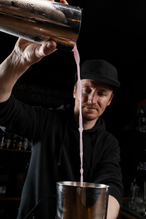 Bartender mixes egg white, lemon, dry vermouth and gin to prepare the Clover club cocktail. Barman prepares classical Clover club alcoholic cocktail at the bar.の写真素材