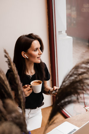 Girl manager with laptop and cup of coffee have online video meeting with colleagues and business partners. Team discussion trends and tasks. Problem solving remotelyの写真素材