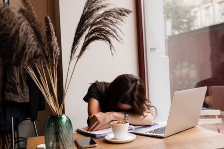 Sleeping girl with laptop on the table in loft cafe. Tired young woman with closed eyes have a break...