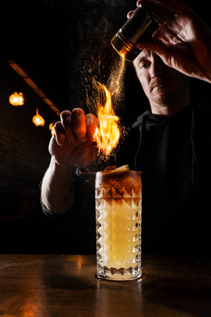 Burning cinnamon in cocktail. Bartender pours and fire burns cinnamon in alcoholic cocktail at a bar. Bartender is preparing alcoholic cocktail with whiskey, fresh lemon, sugar syrup and egg whiteの写真素材